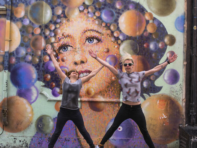 Two people jumping in front of graffiti