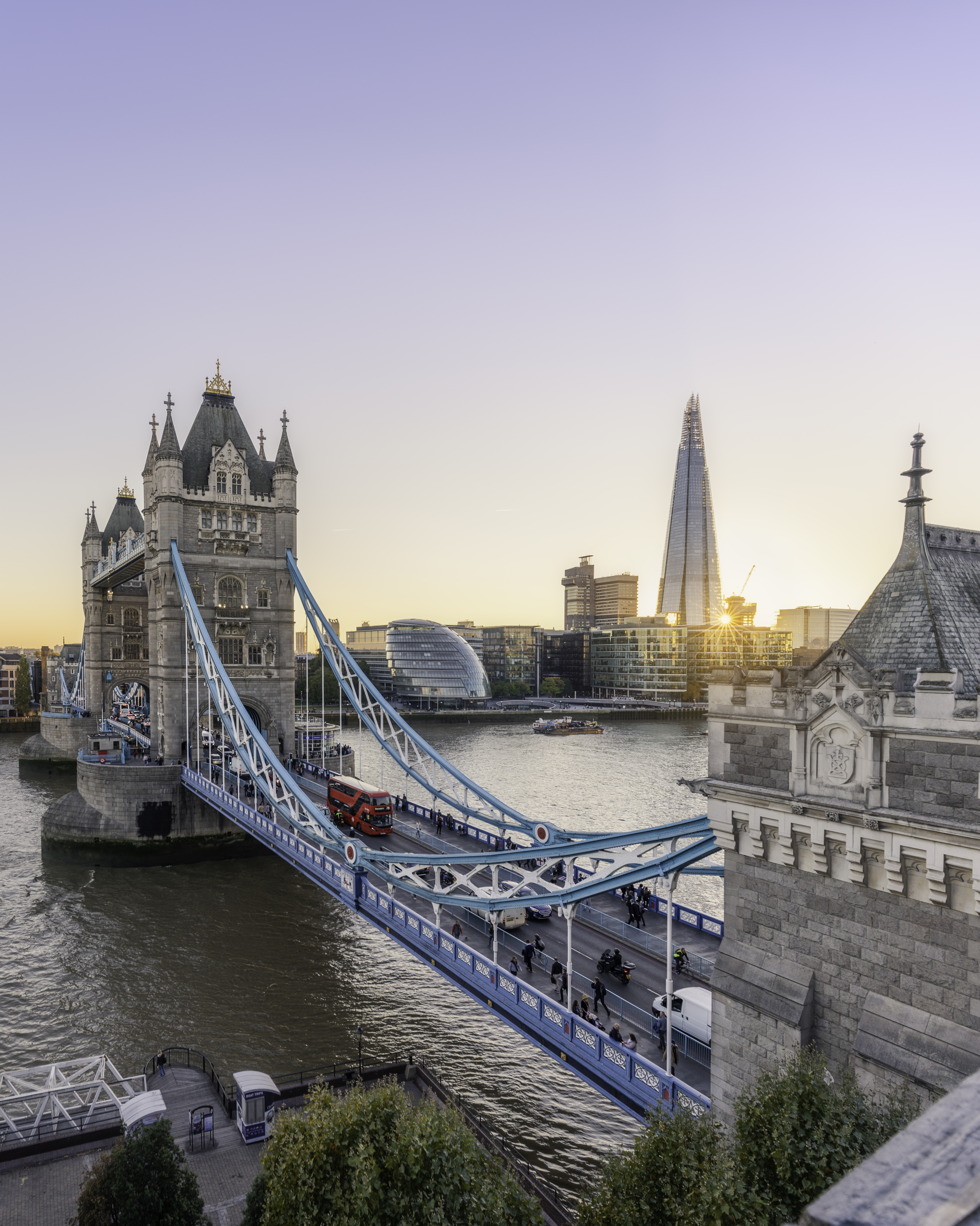 View of Tower Bridge and Shard at sunset, with a red bus going across the bridge.