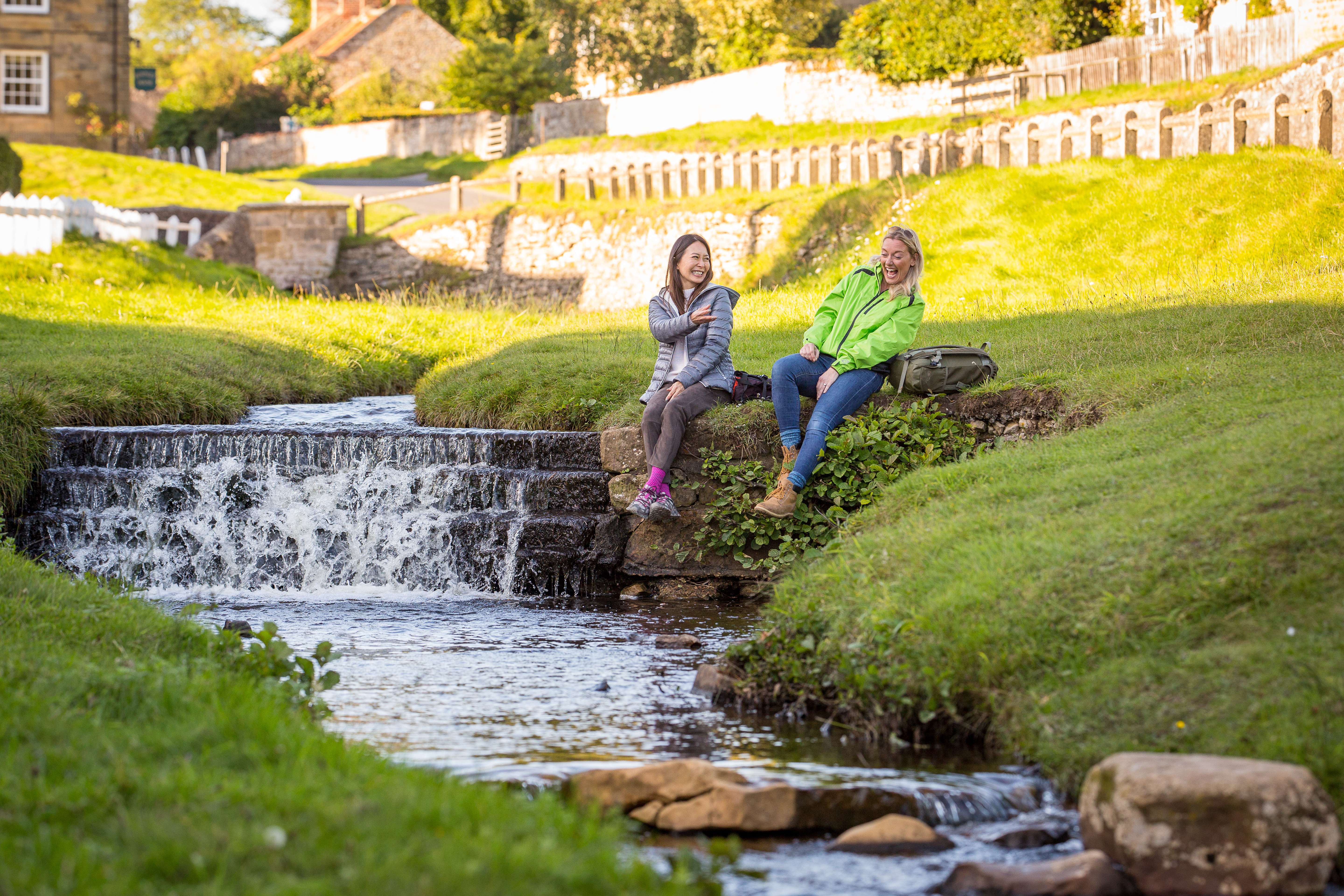 Two women sat on the banks of a stream, in a village