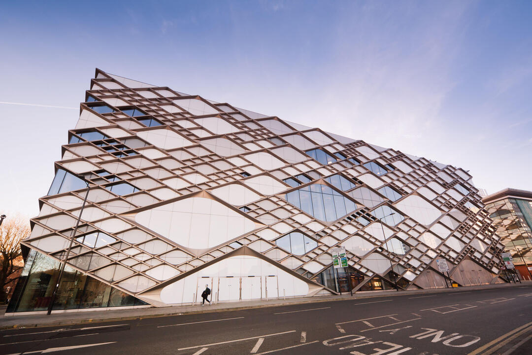 Modern building with geometric facade, featuring crisscrossing diamond shapes, glass panels, and a city street in front.