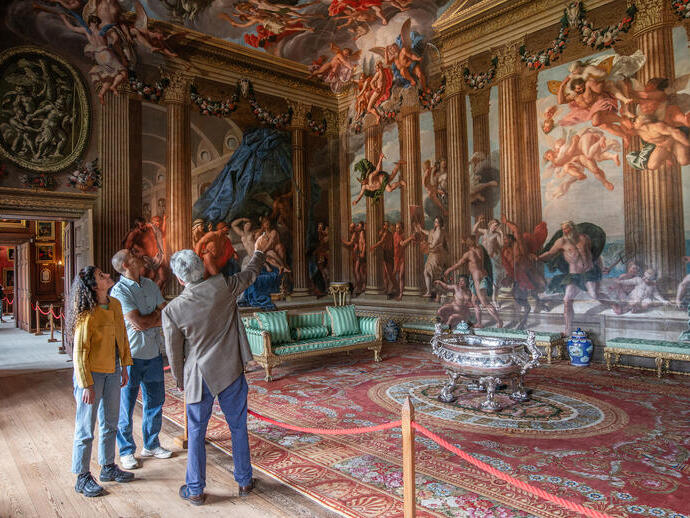 A man and a woman with a tour guide in an ornate room with paintings
