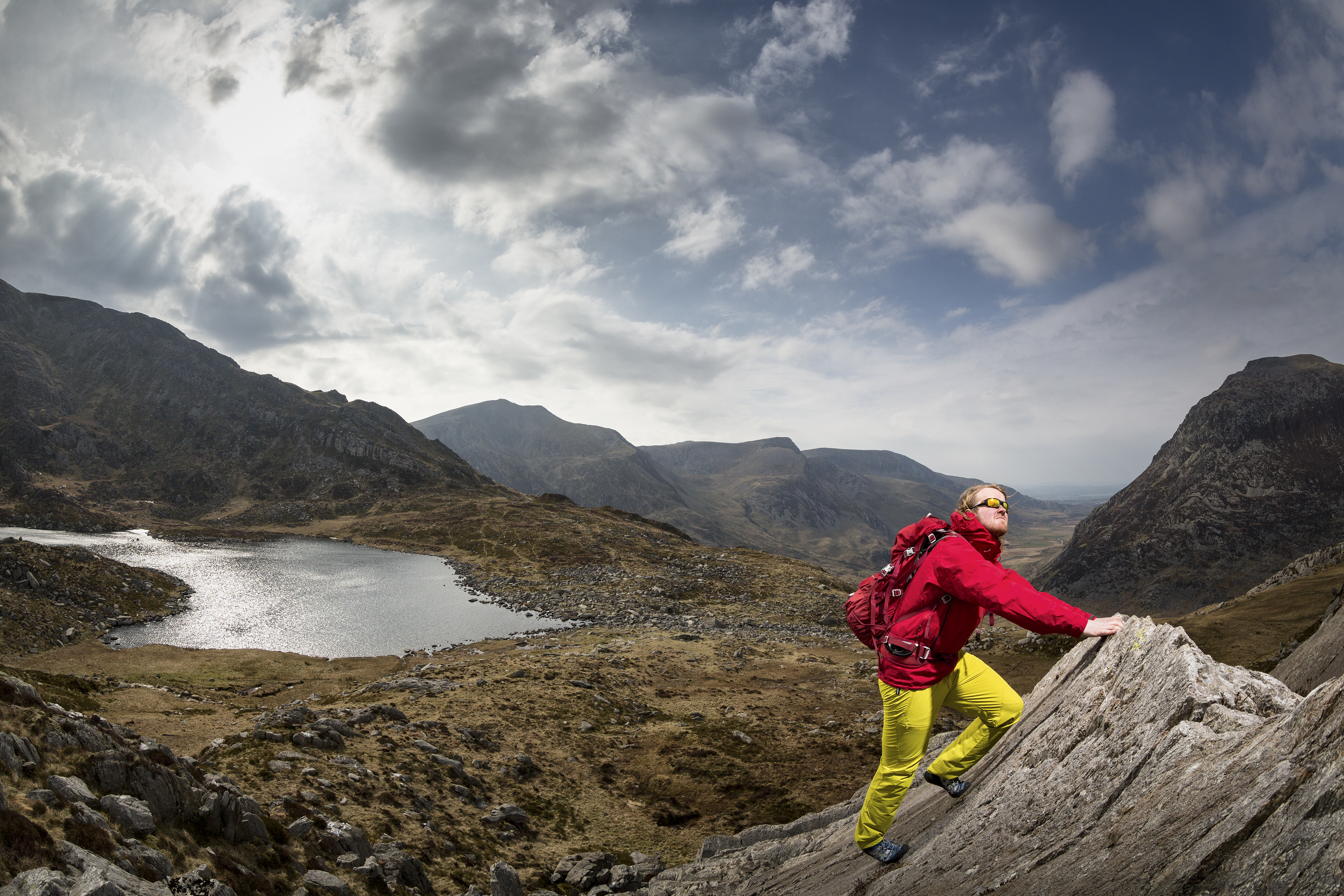 A man climbing a sharp rock formation overlooking a lake