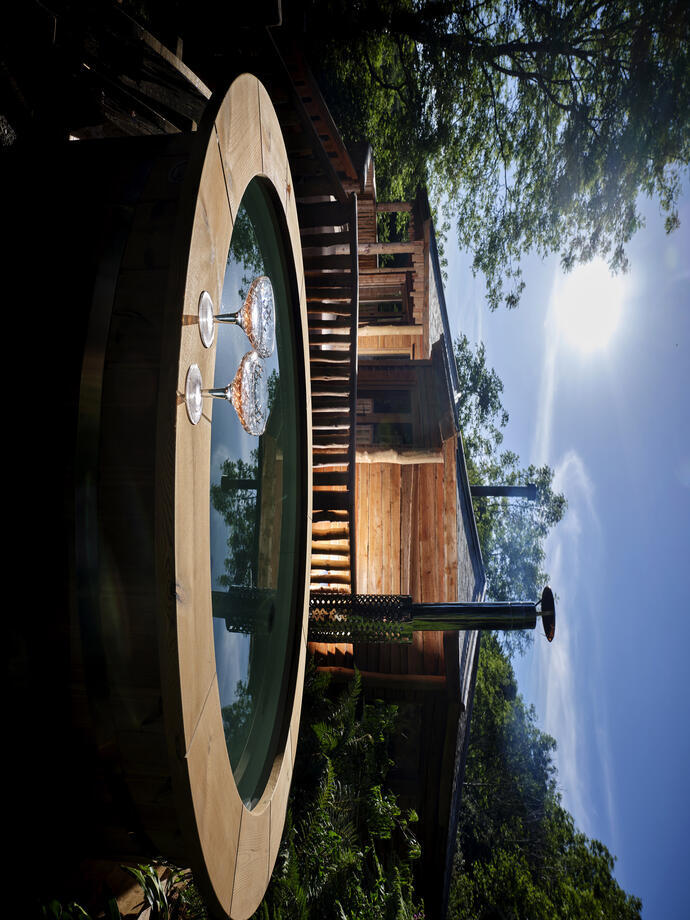 A wooden edged hot tub in front of the lit wooden lodge at Sleepy Owl Devon.