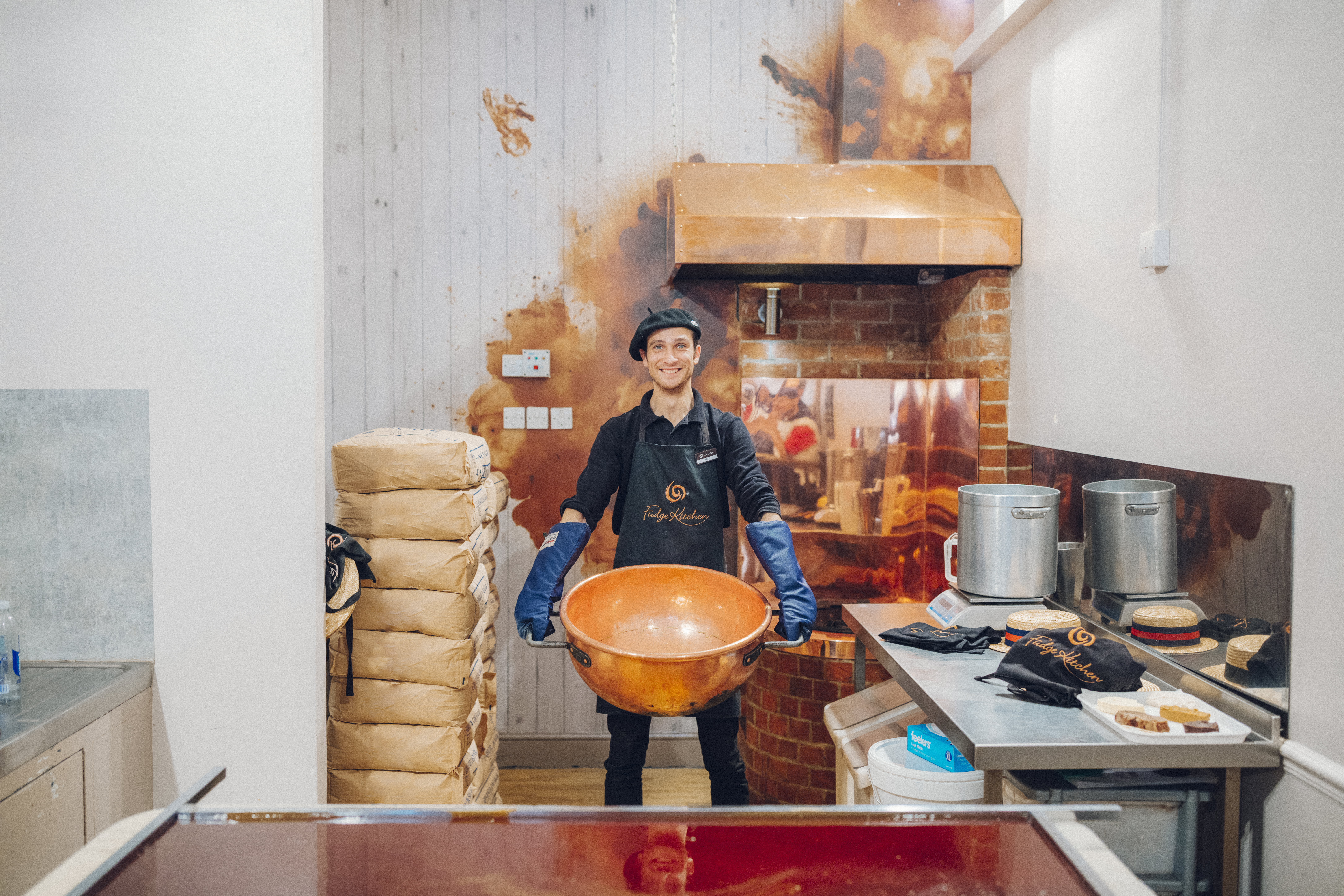 Man in a beret and protective clothing holding a large copper pan