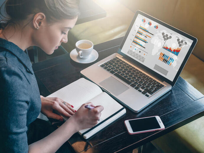 Young business woman sitting at table and taking notes in notebook