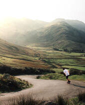 Man skateboarding down a road through a deep valley in the sunshine