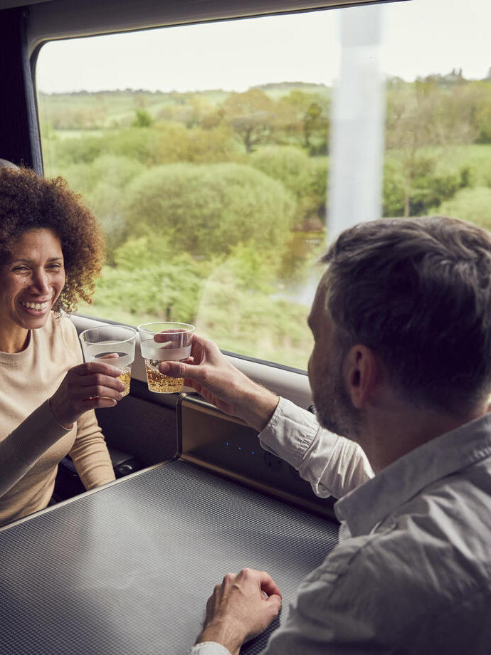 Una pareja disfrutando de una copa mientras viaja en tren desde Bath, sentados en una mesa, brindando