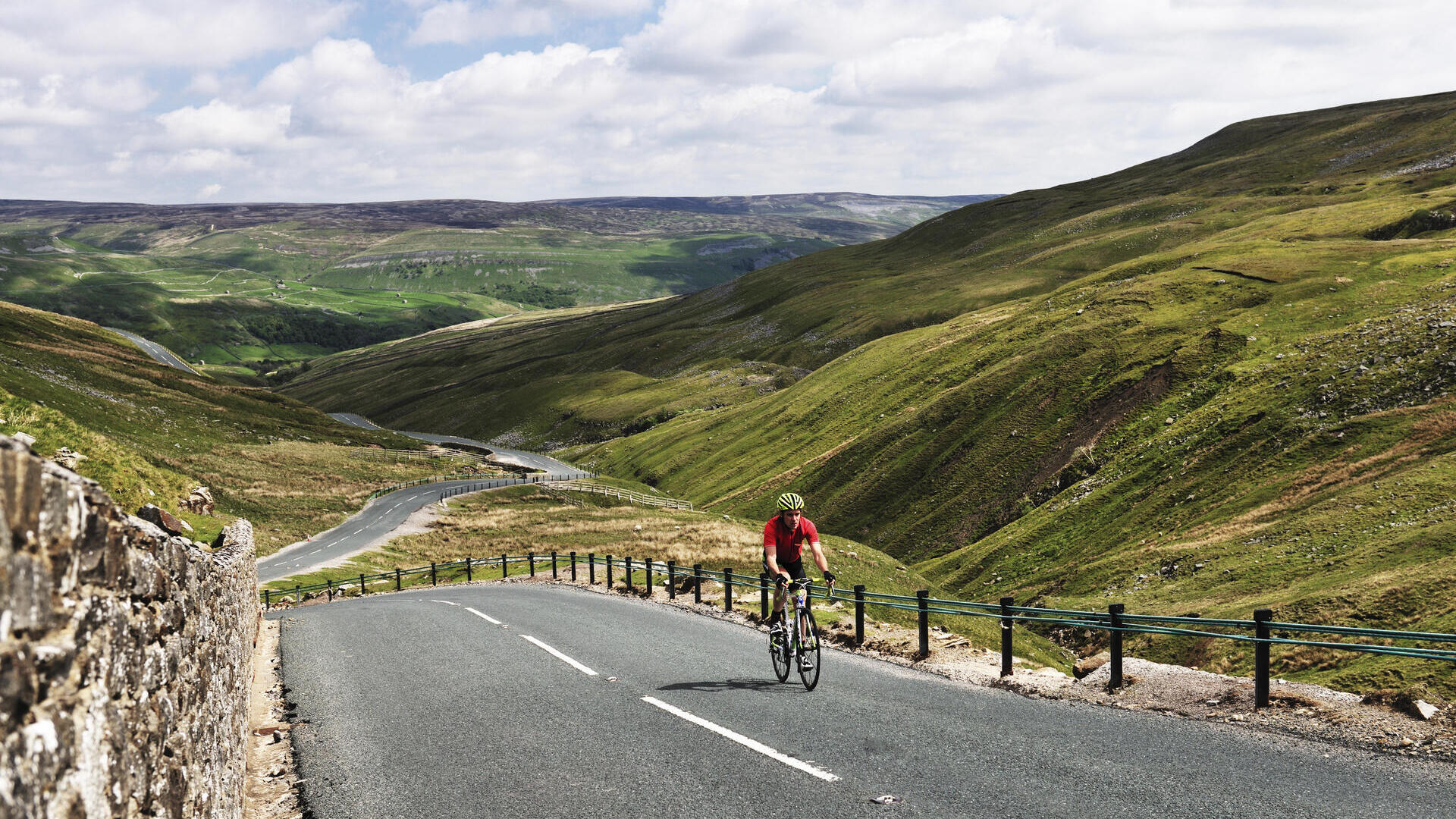 Cyclist riding on road through green dales