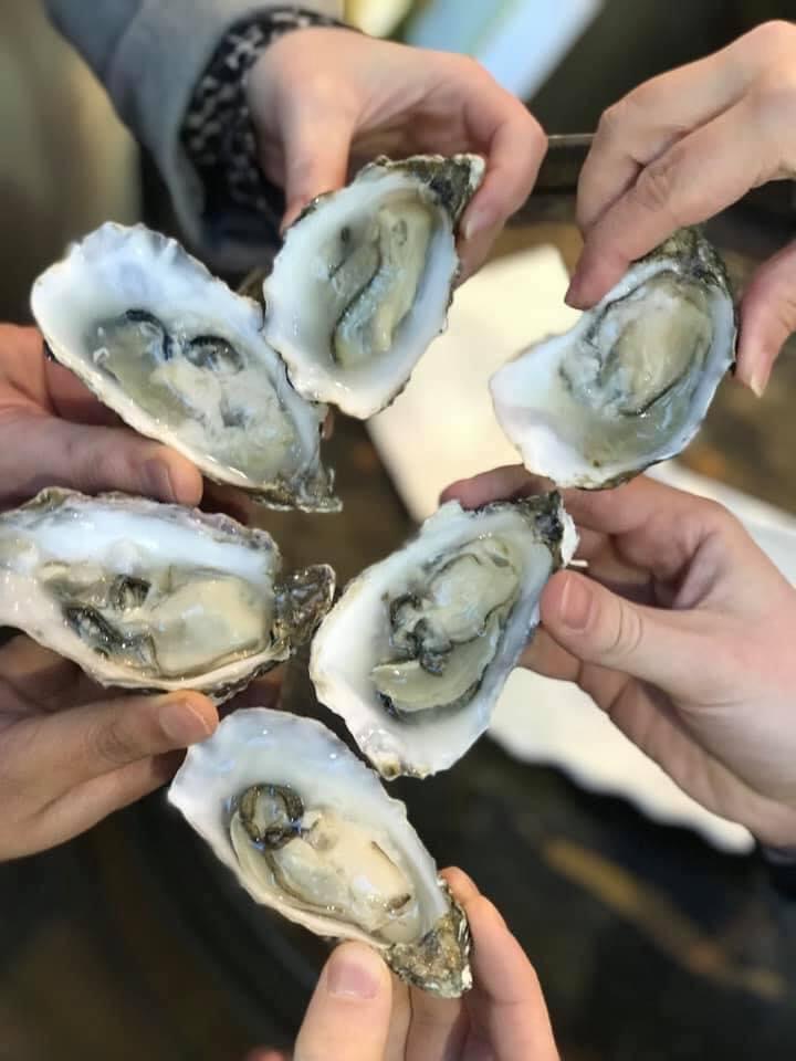 Close-up of six hands holding open oyster shells complete with oysters, ready to eat 