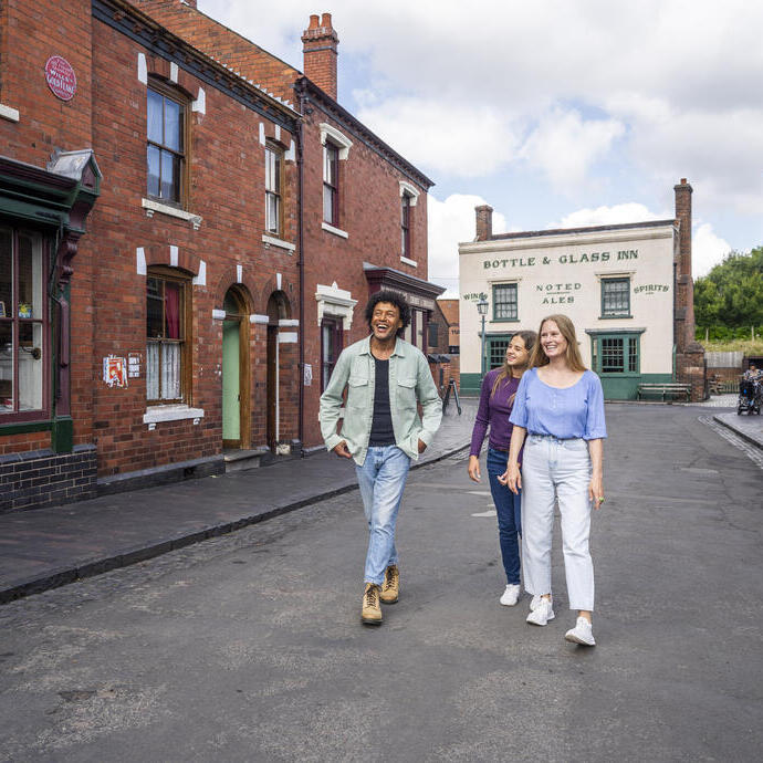 Three people walking and smiling in a historic-looking street with red brick buildings and a pub in the background.