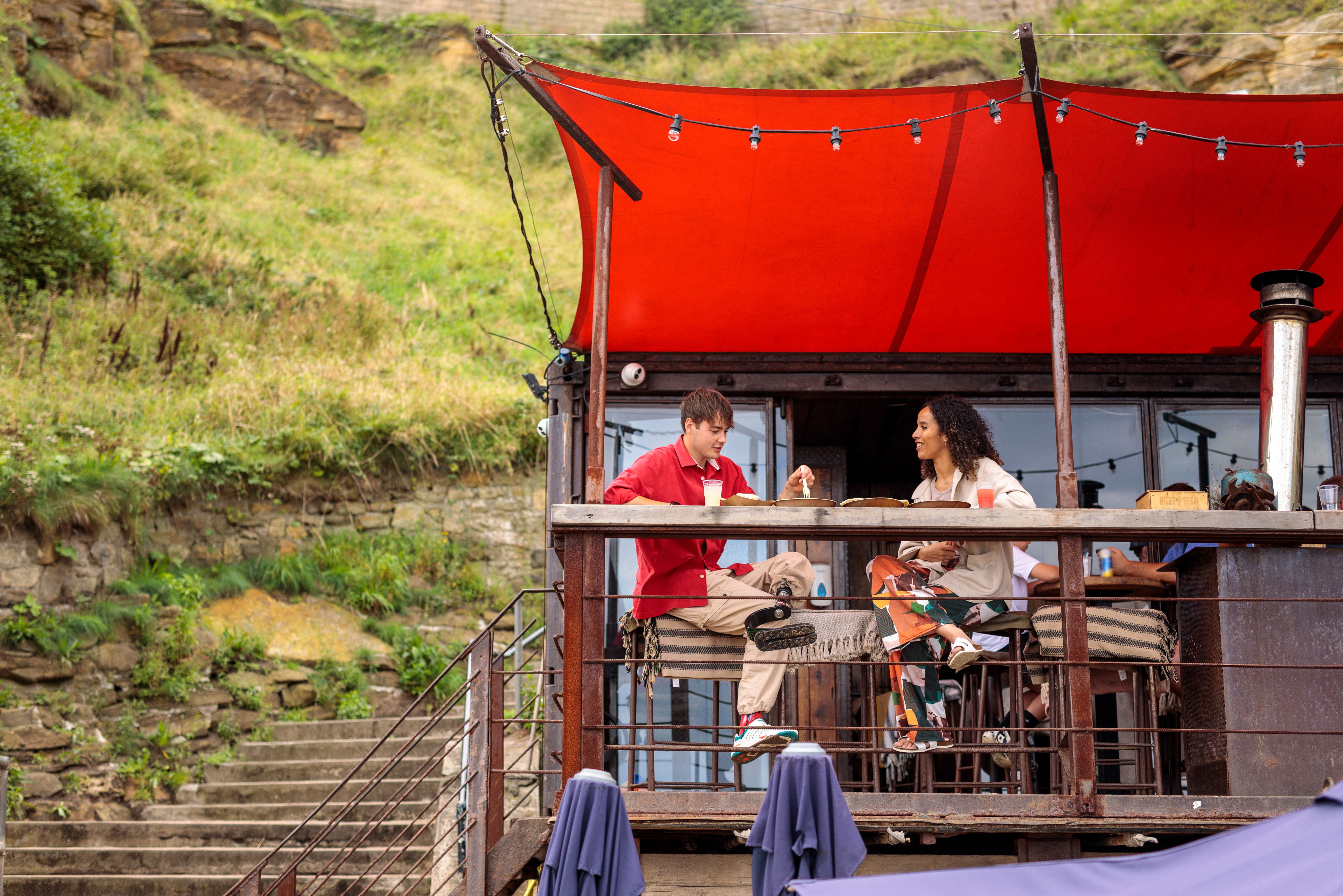 Friends enjoying food and drink at a beachside outdoor cafe.