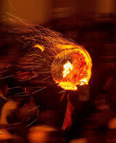 Des participants courent dans les rues avec un baril de goudron enflammé.