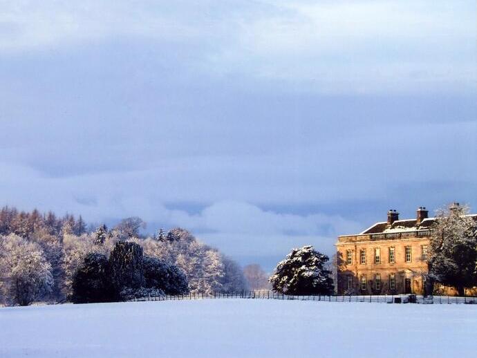 Large historic building on snowy landscape with trees and dramatic winter sky, evoking a peaceful and serene atmosphere.