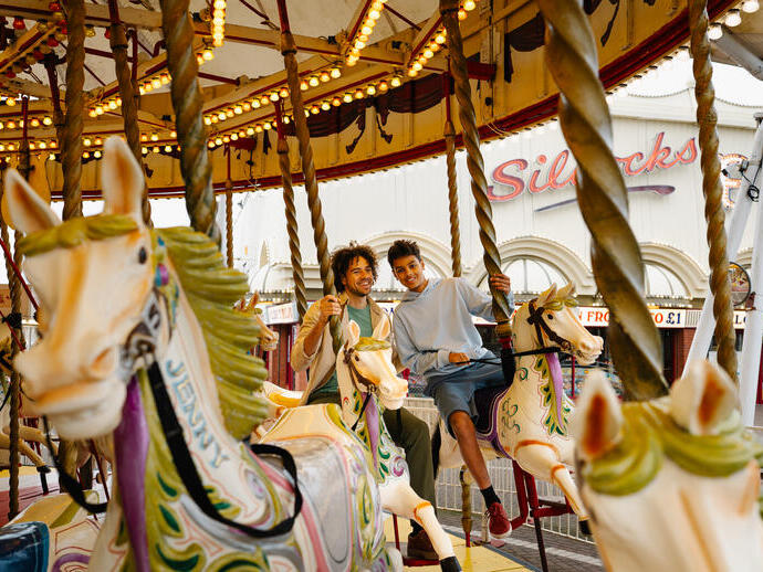 Two people riding on carousel horses at an amusement park.