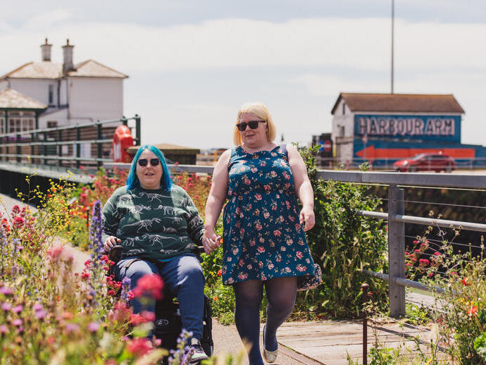 A woman walks with another women who sits in a wheelchair at an old railway station