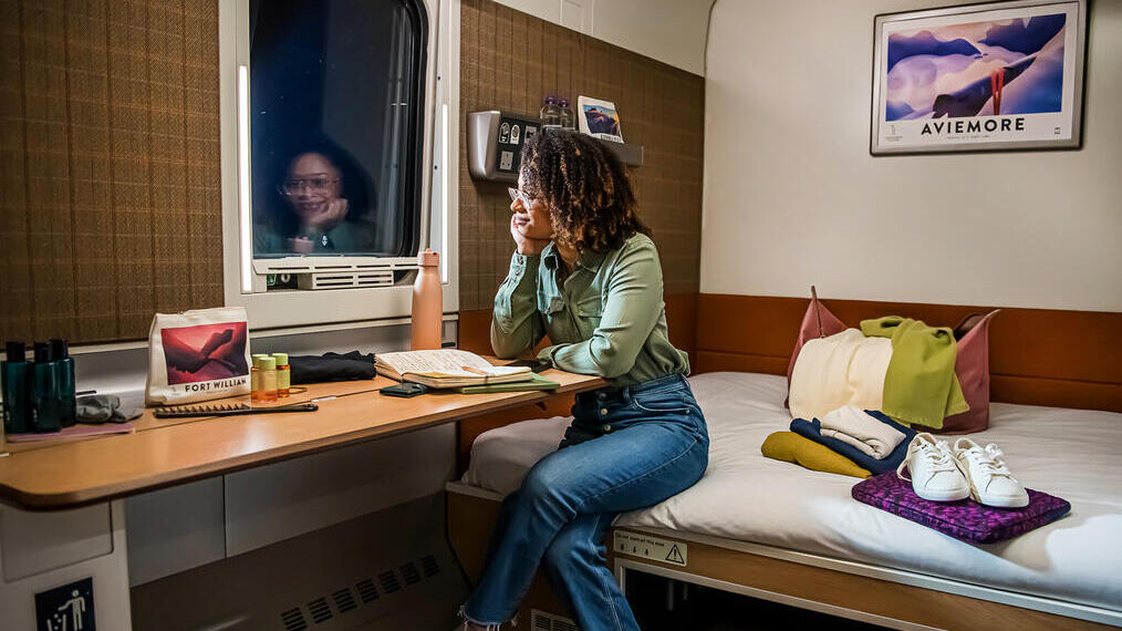 Woman smiling sitting on bed and looking out of the window on the Caledonian Sleeper