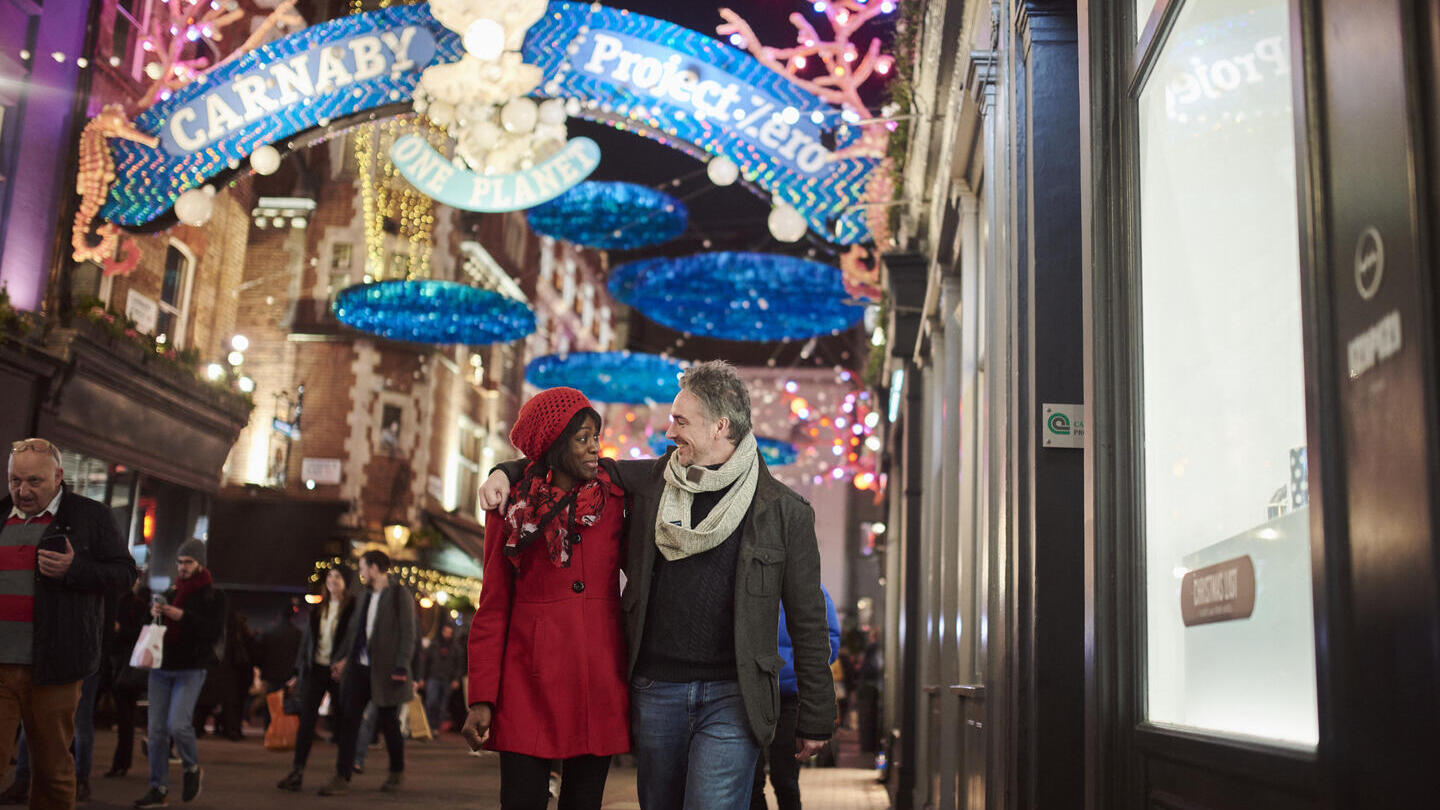 Paar, das unter Weihnachtsbeleuchtung die Straße entlanggeht