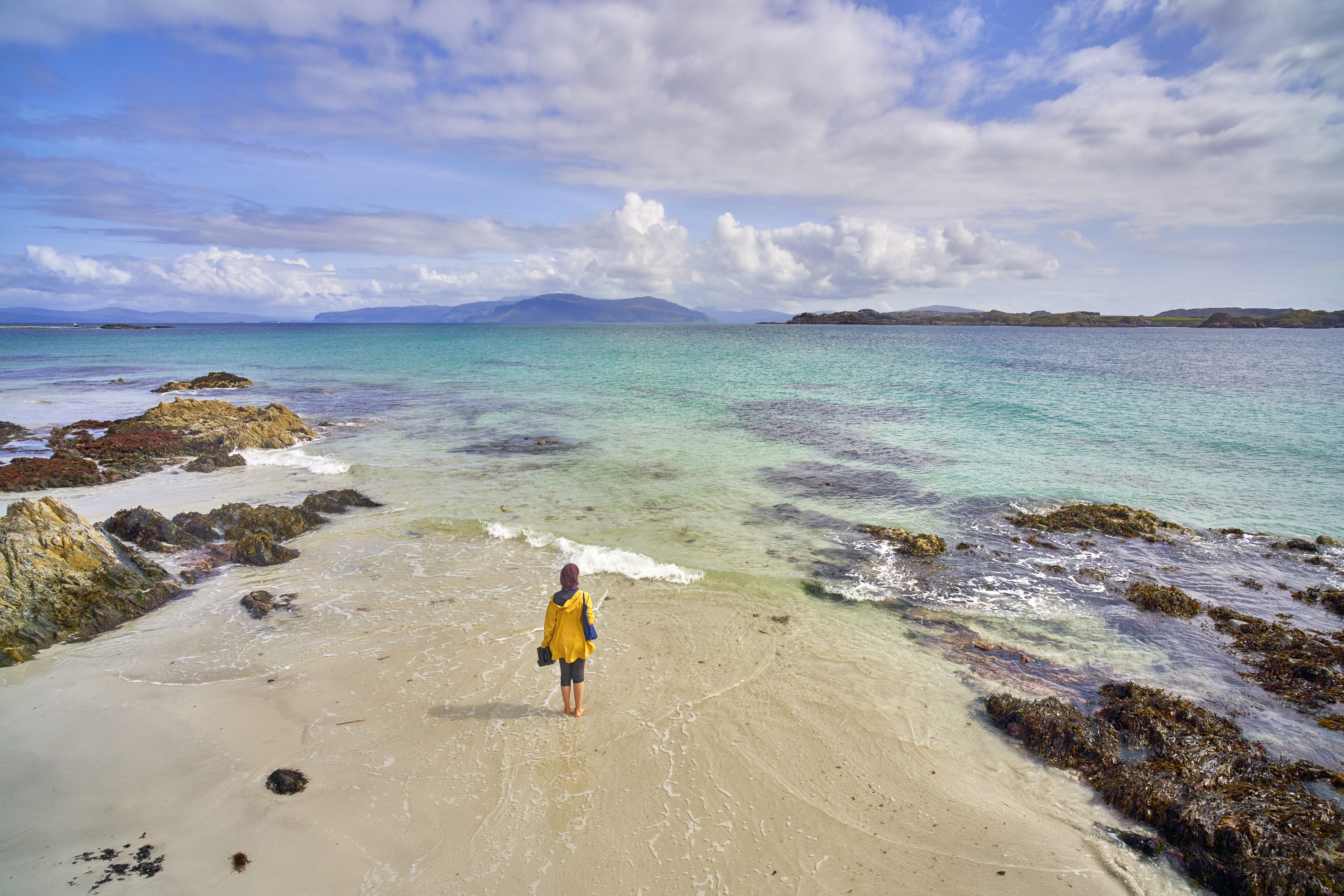 Eine junge Frau, die auf dem weißen Sandstrand mit kristallklarem, blauem Wasser spazieren geht.