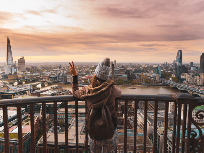 Woman on a balcony at the top of a high building looking over a city
