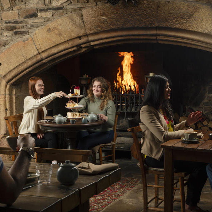 Two women enjoy an Afternoon Tea in front of a fire in an traditional historic pub