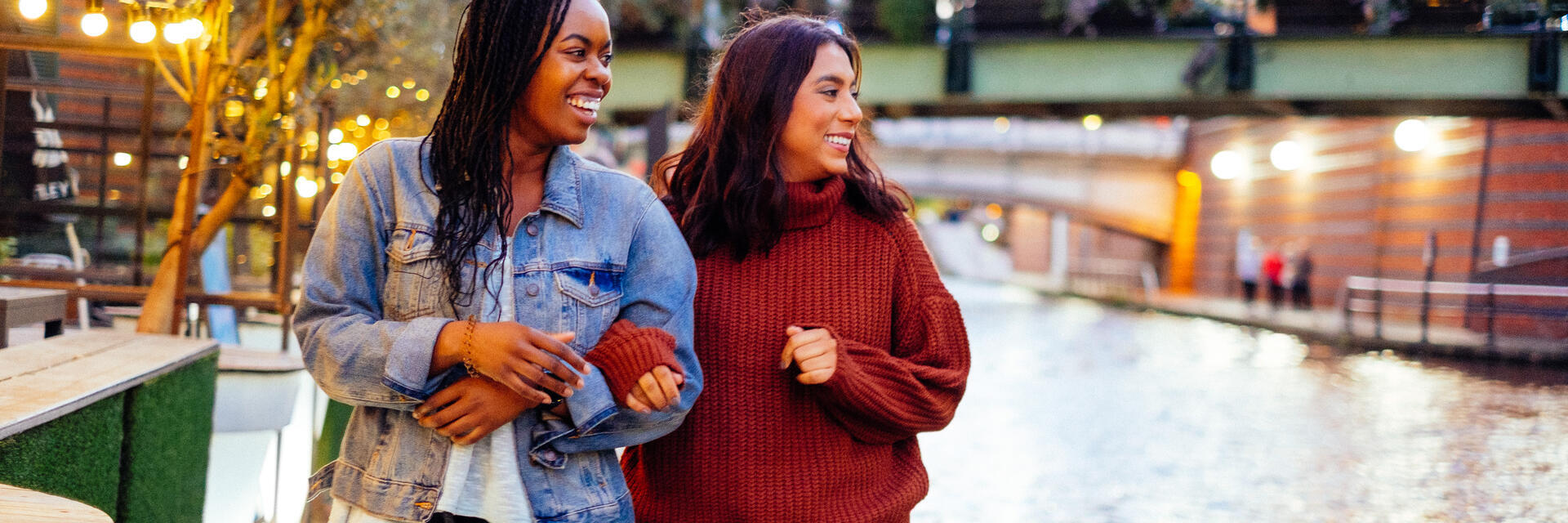 Two women, linking arms, walking beside a canal in evening