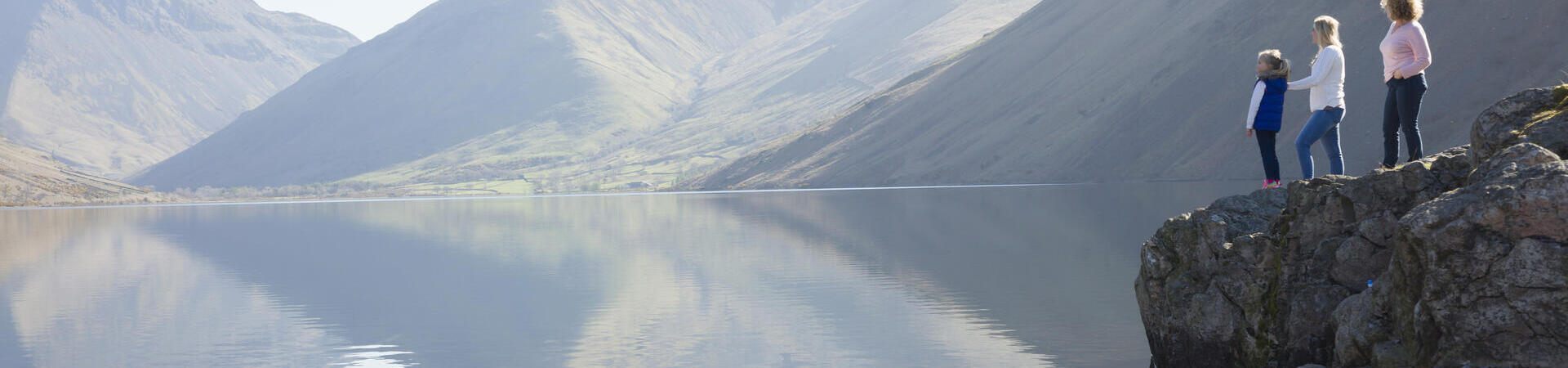 Two women and child standing on a rock overlooking lake