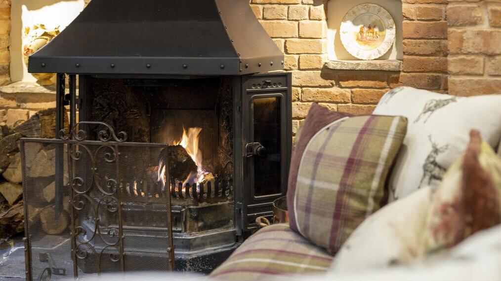 Close-up of the inglenook fireplace with fire and tartan patterned sofas.