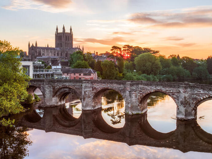 Puente romano sobre un río con una catedral al fondo al amanecer