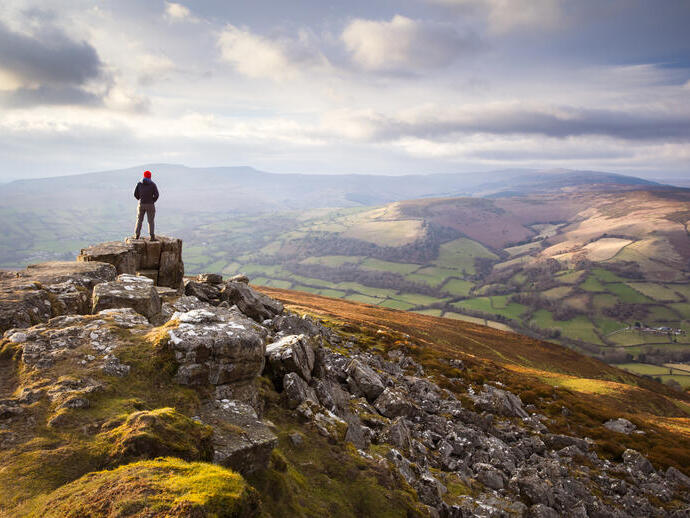 Un homme au sommet d'une vaste chaîne de montagnes colorée au coucher du soleil, regardant vers la vallée