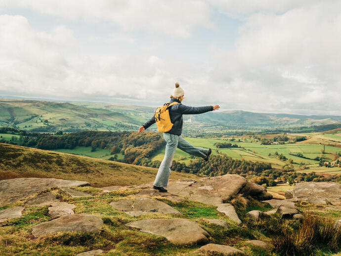 Woman skipping on rocks at edge of hill. Landscape view