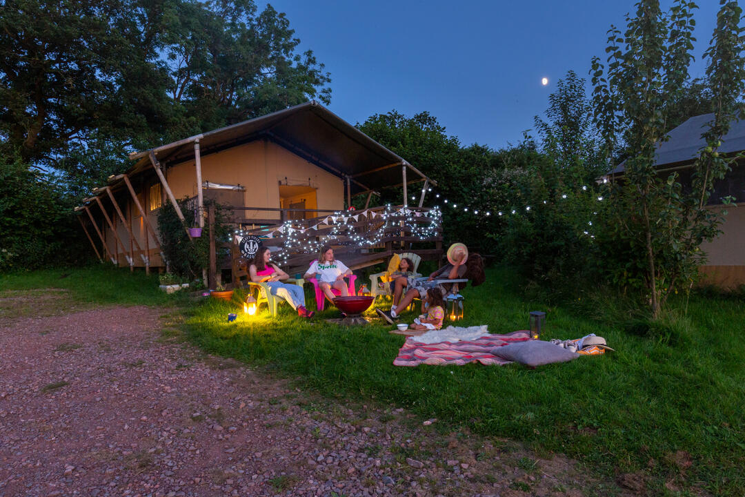 Group of campers sitting in a garden outside a hut at a glamping site