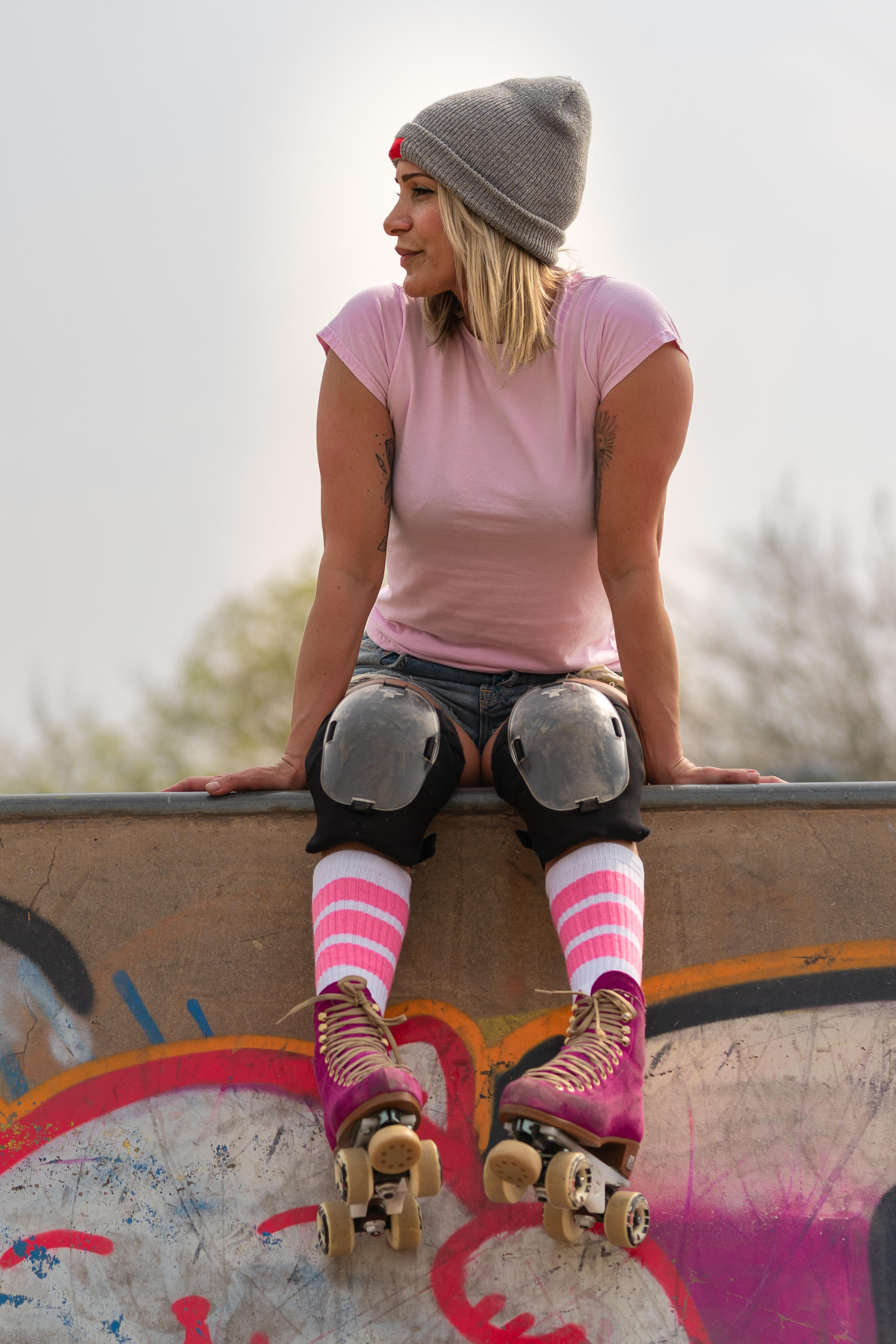A young woman in rollerskates sitting on the edge of a skate park.