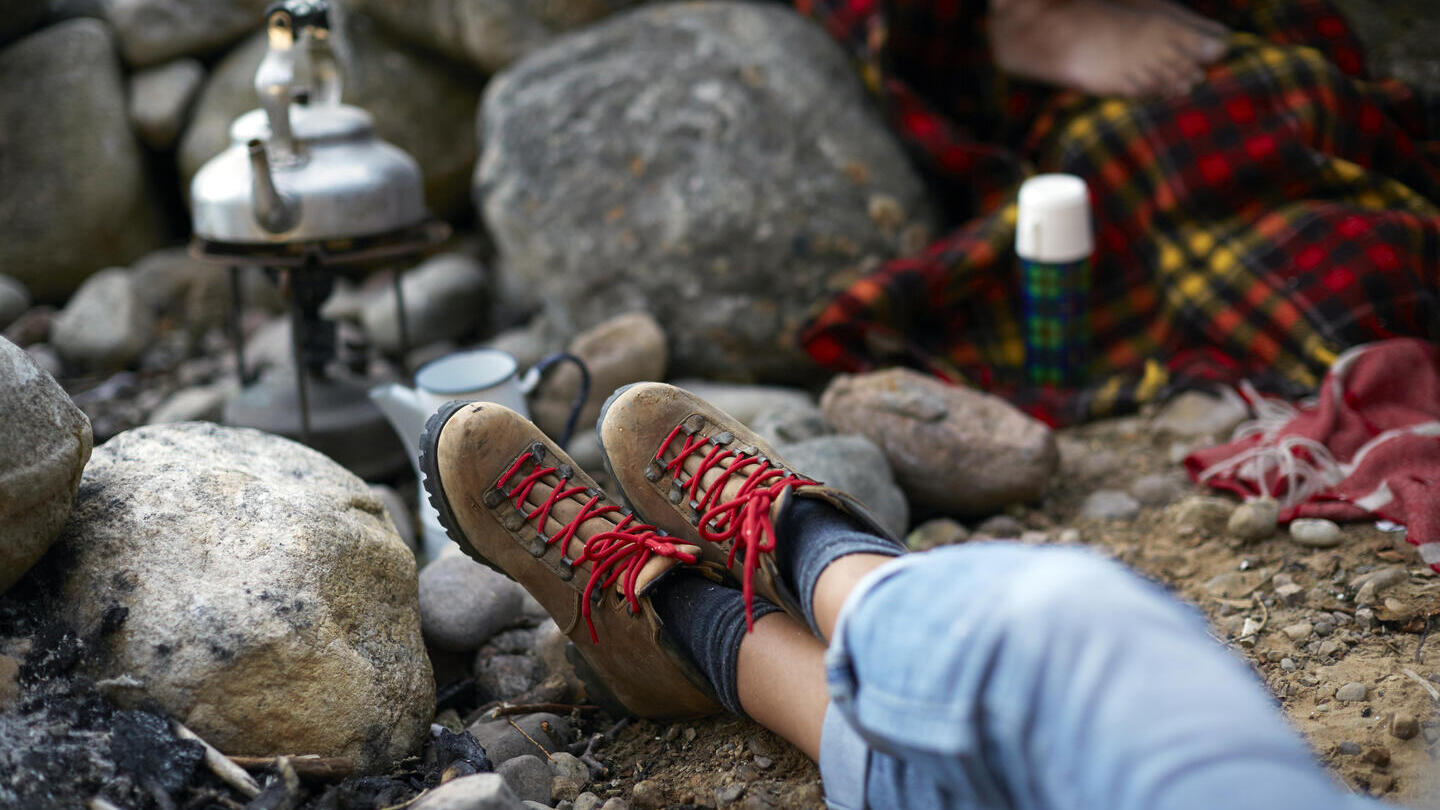 Woman sitting on a rocky ground, with legs outstretched waiting for a kettle to boil