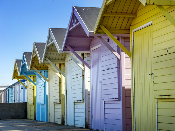 Row of colourful beach huts with blue sky above.