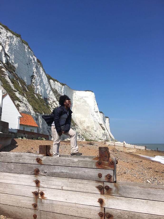 Frau, die auf Holzpfählen an einem Strand mit weißen Klippen im Hintergrund steht