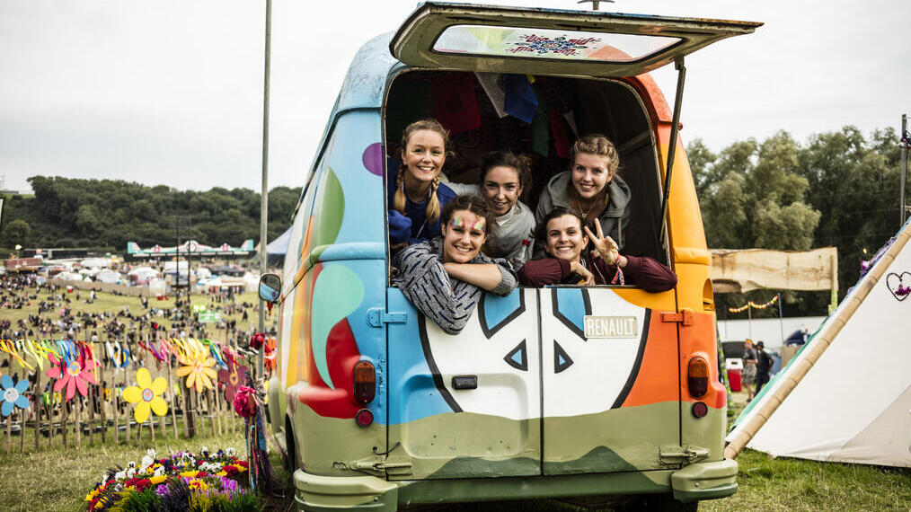 Group of friends smiling out of the back of a rainbow van