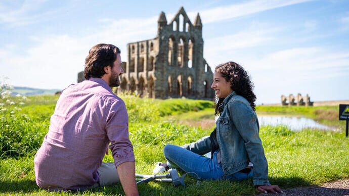Man and woman sitting on grass with crutches beside them, an Abbey in the background