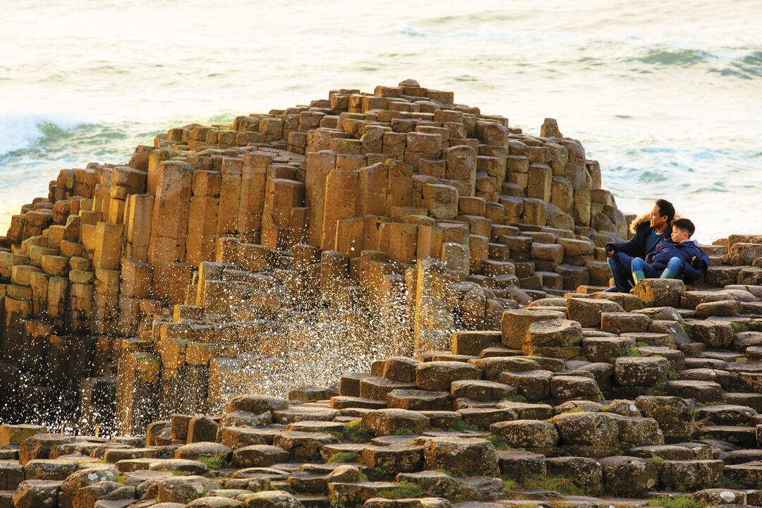Man and child sitting on rock formations by the sea