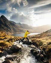 Man jumping from rock to rock across a stream flowing into a lake