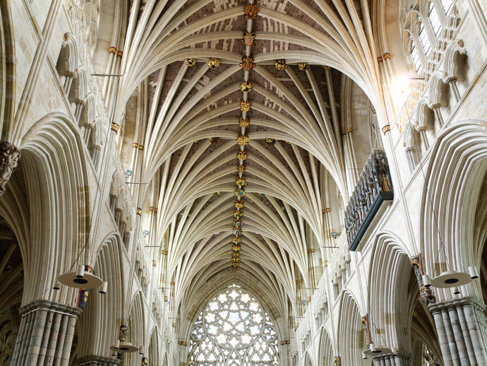 Das Gewölbe einer gotischen Kathedrale mit kunstvollen Steinmetzarbeiten und dekorativen Schlusssteinen, vom Kirchenschiff aus gesehen.
