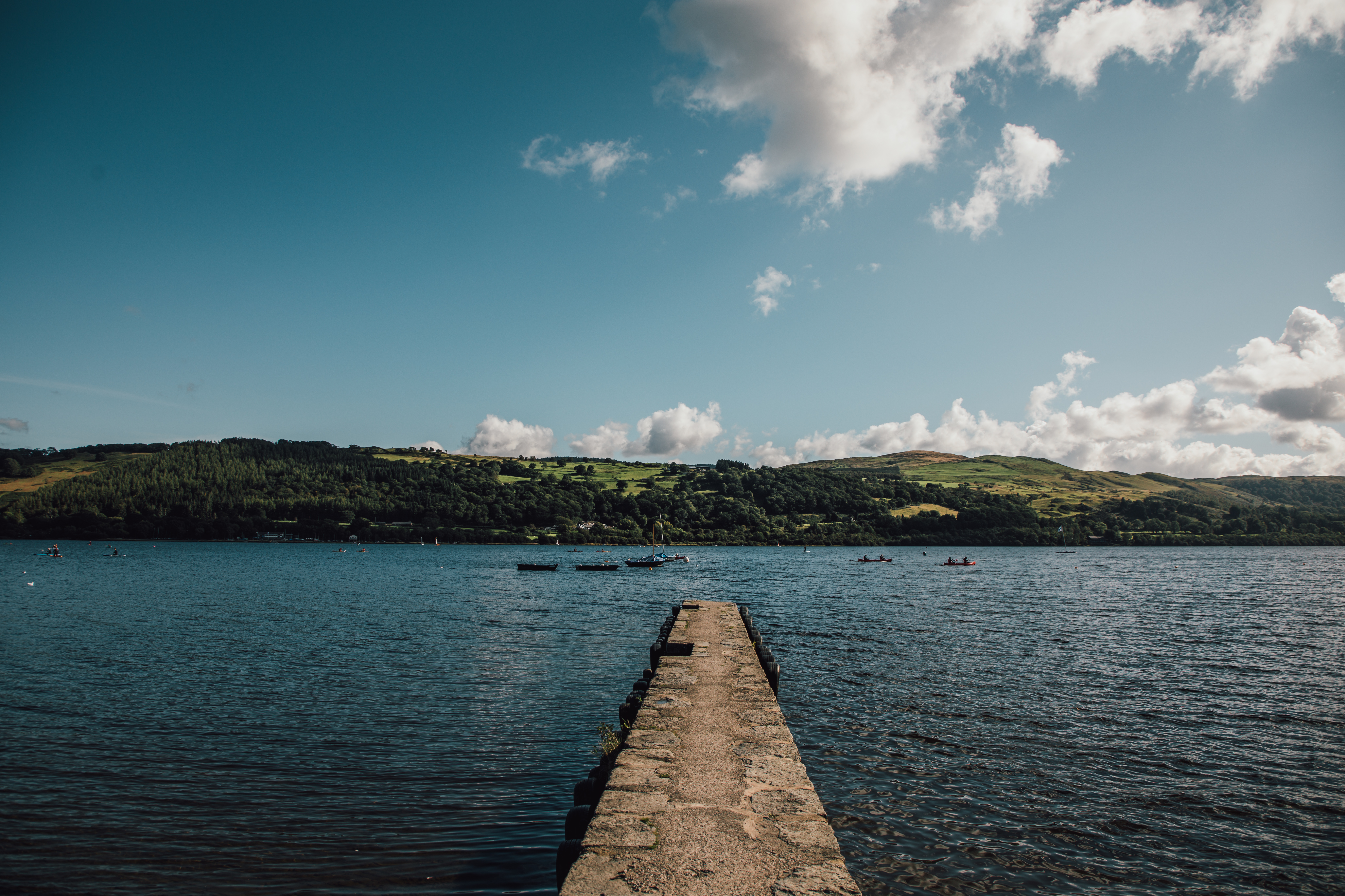 A pier jetting out into a lake in Snowdonia/Eryri National Park with boats passing in the distance