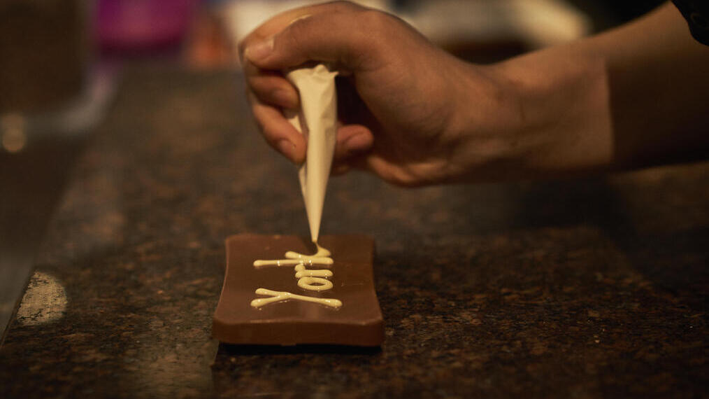 Person decorating dark chocolate with white chocolate piping