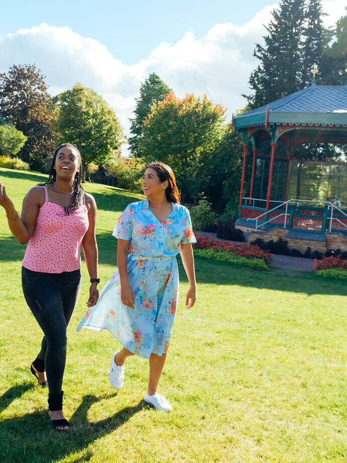 Two women walking on grass past a pergola