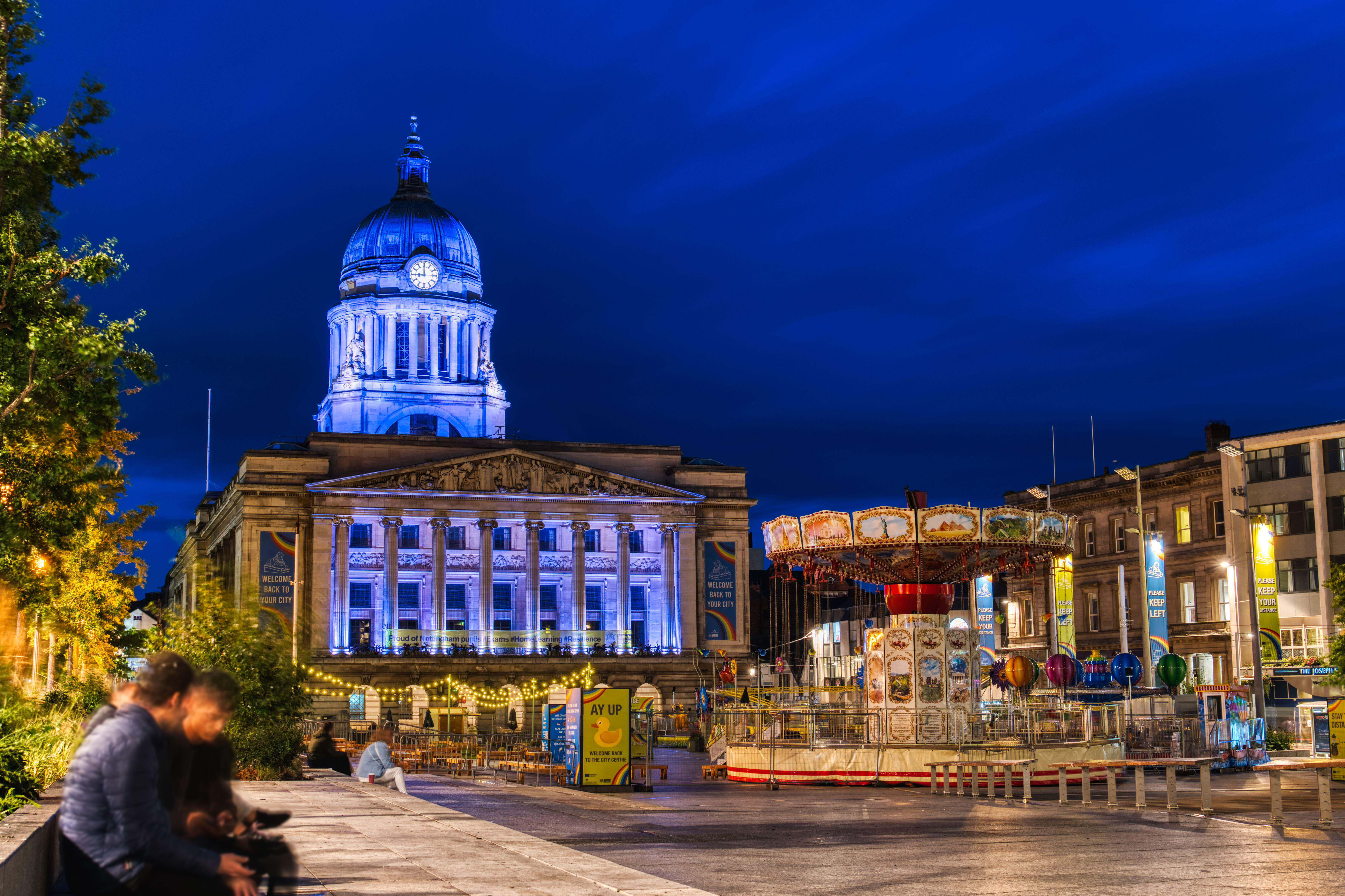 Evening view of city square with large municipal building and a merry go round.