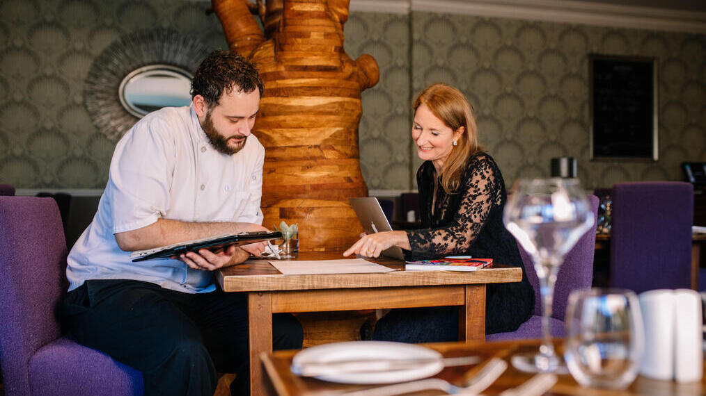 Head Chef and female nutritionalist sat in empty restaurant discussing menu plans for The Green House Hotel, Bournemouth