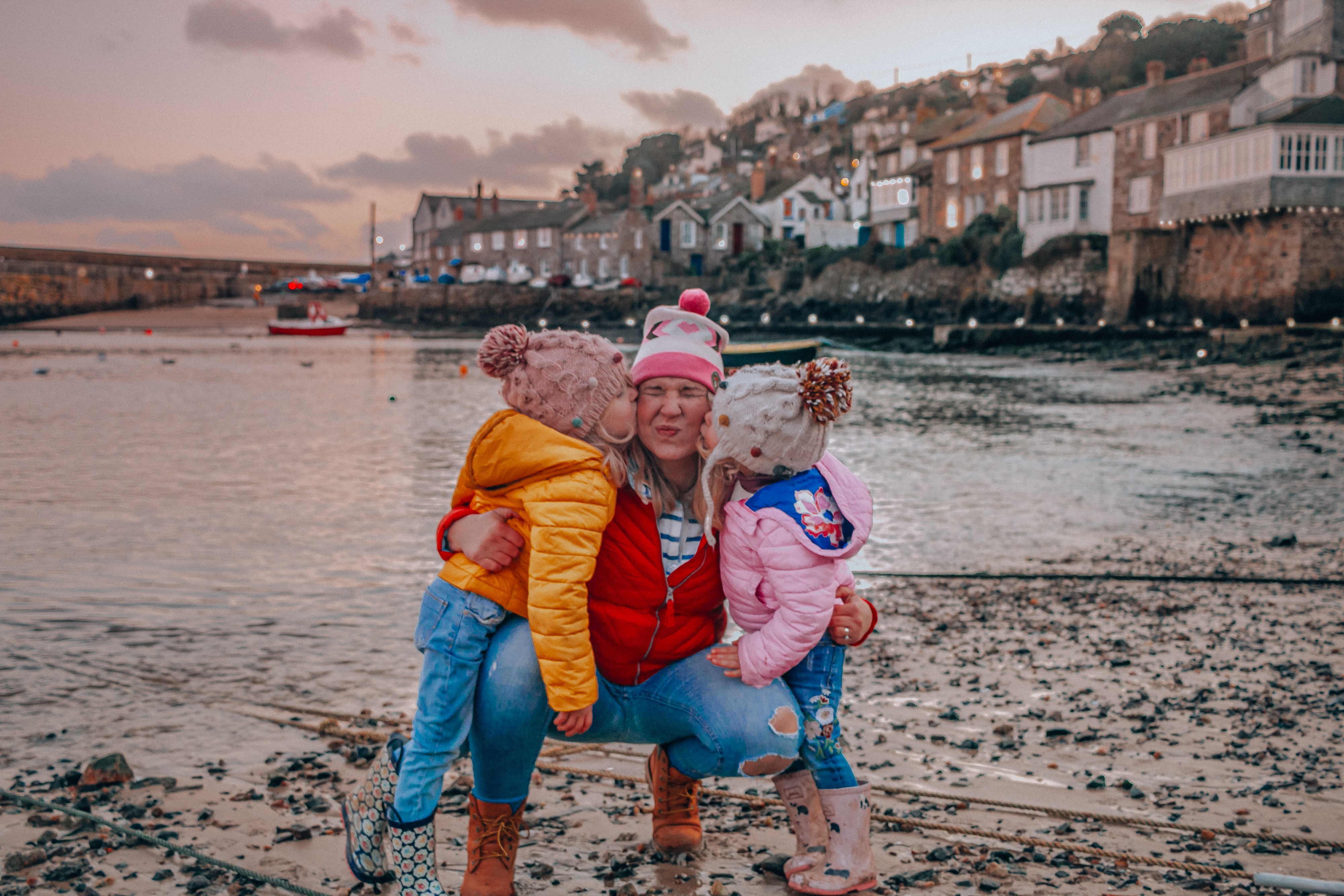 Two children giving a woman a kiss on the cheek on a beach