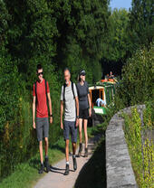 Three people walking on a path along a canal with boats moored.
