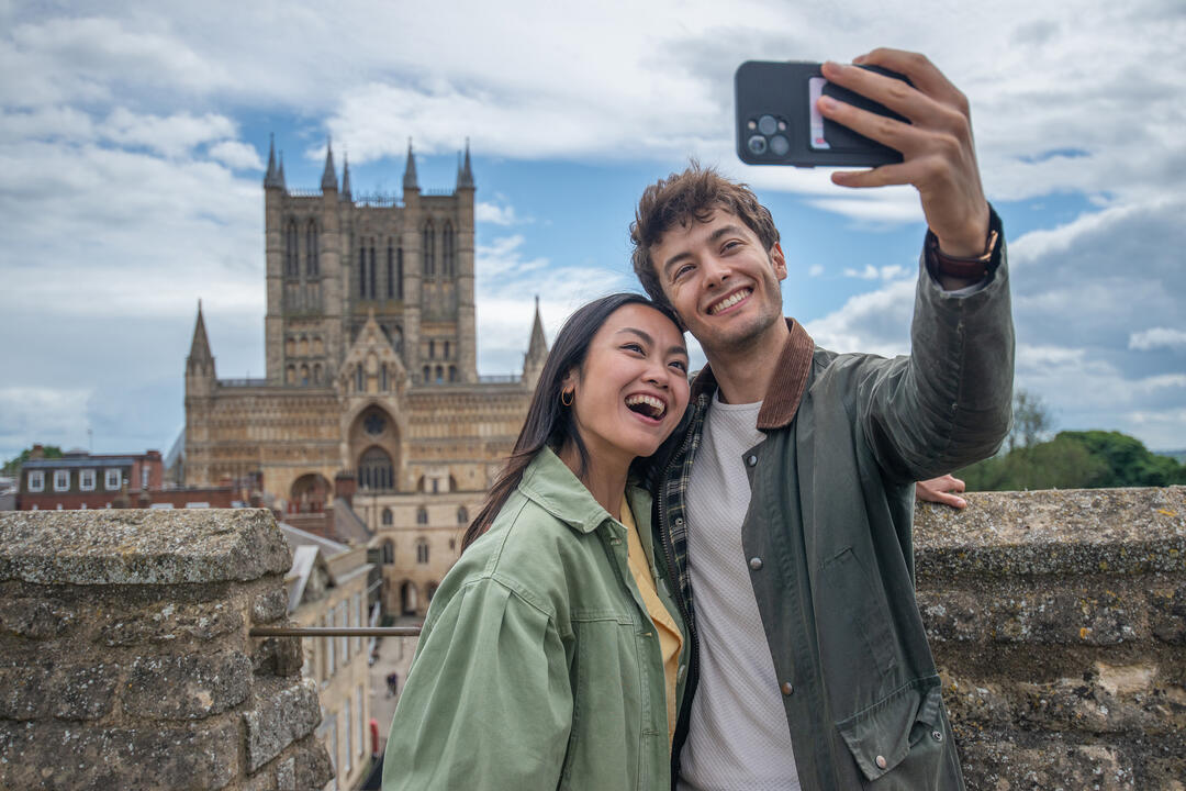 A man and woman smiling and taking a selfie in front of a Cathedral