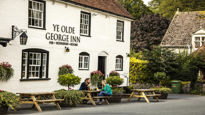 A couple sitting outside a pub on a bench having a drink and eating a meal