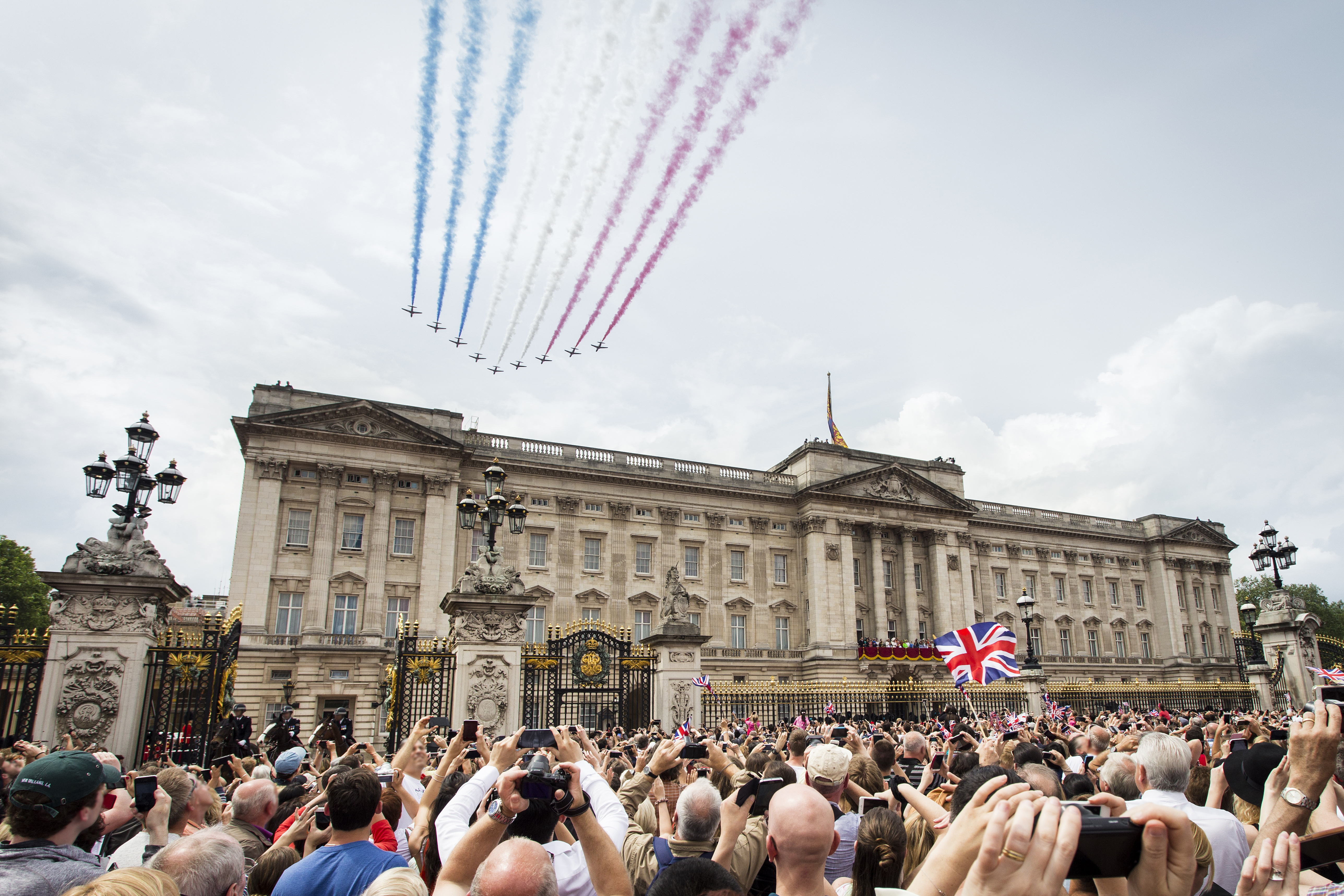 Jets with coloured smoke trailing behind fly in formation over crowds and a palace